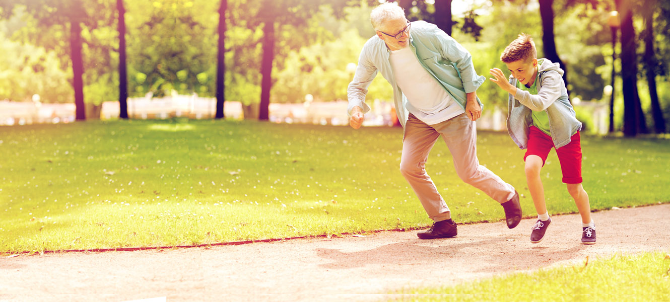 Grandfather and grandson racing each other in a park.